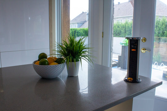 Comptoir de cuisine moderne Vision Renov en quartz gris, décoré avec une plante verte, un bol de fruits et une tour de prises électriques. Vue sur une porte vitrée donnant sur un jardin. Germoir-03.